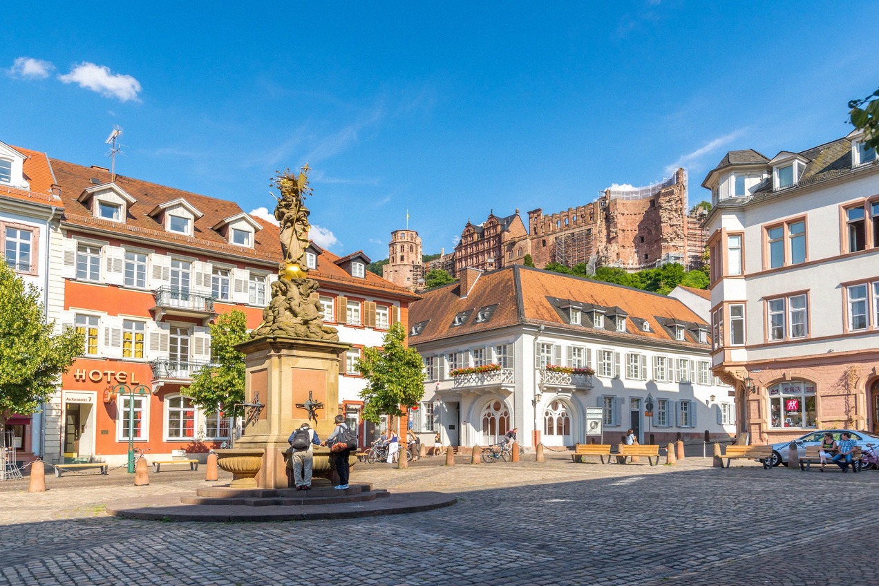 Der Kornmarkt in der Heidelberger Altstadt mit Mariensäule und Blick auf das mächtige rote Sandsteinschloss über den Dächern der Stadt