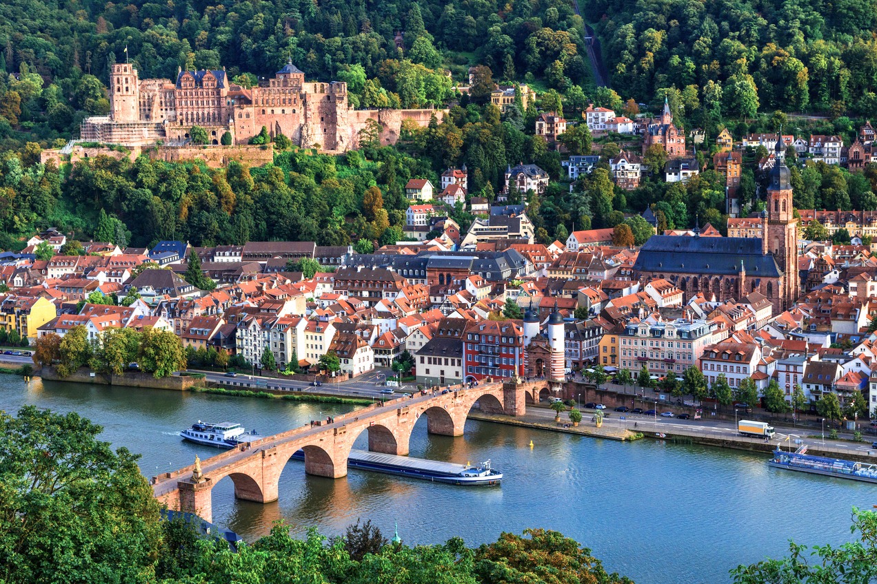 Klassische Heidelberg-Ansicht: Das rote Schloss auf dem bewaldeten Berghang, die historische Alte Brücke (Karl-Theodor-Brücke) über den Neckar und die…